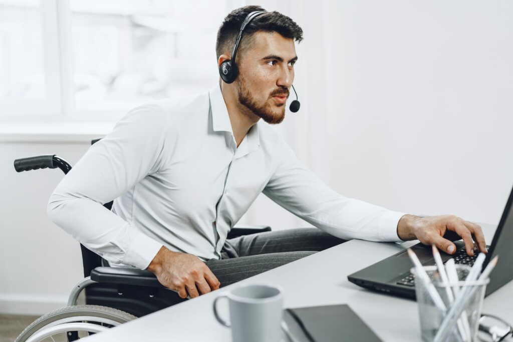 Person using a laptop and headset in a wheelchair, illustrating accessible digital service support.
